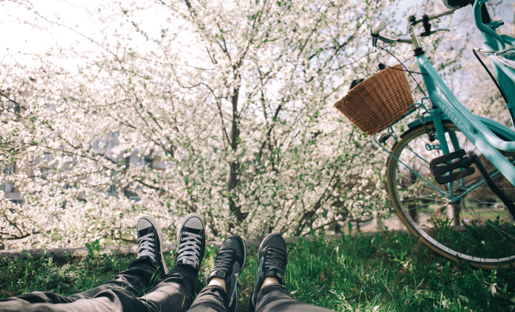 Couple daydreaming at park with feet in grass in front of bloomed tree and blue bike