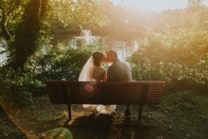 Couple in wedding attire kissing on bench in park