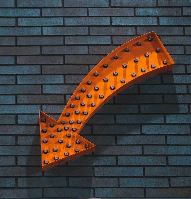 Orange arrow pointing down on dark brick wall