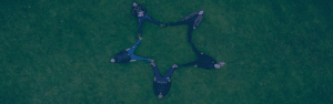 Four people laying on the green grass with legs together making a star shape